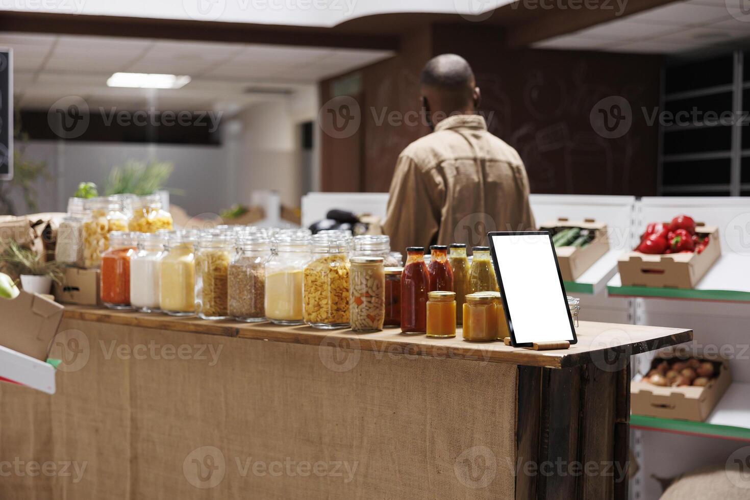 Image showcasing a digital tablet with a blank chromakey mockup template vertically positioned near glass jars. On the counter is a smart device displaying an isolated white screen. photo