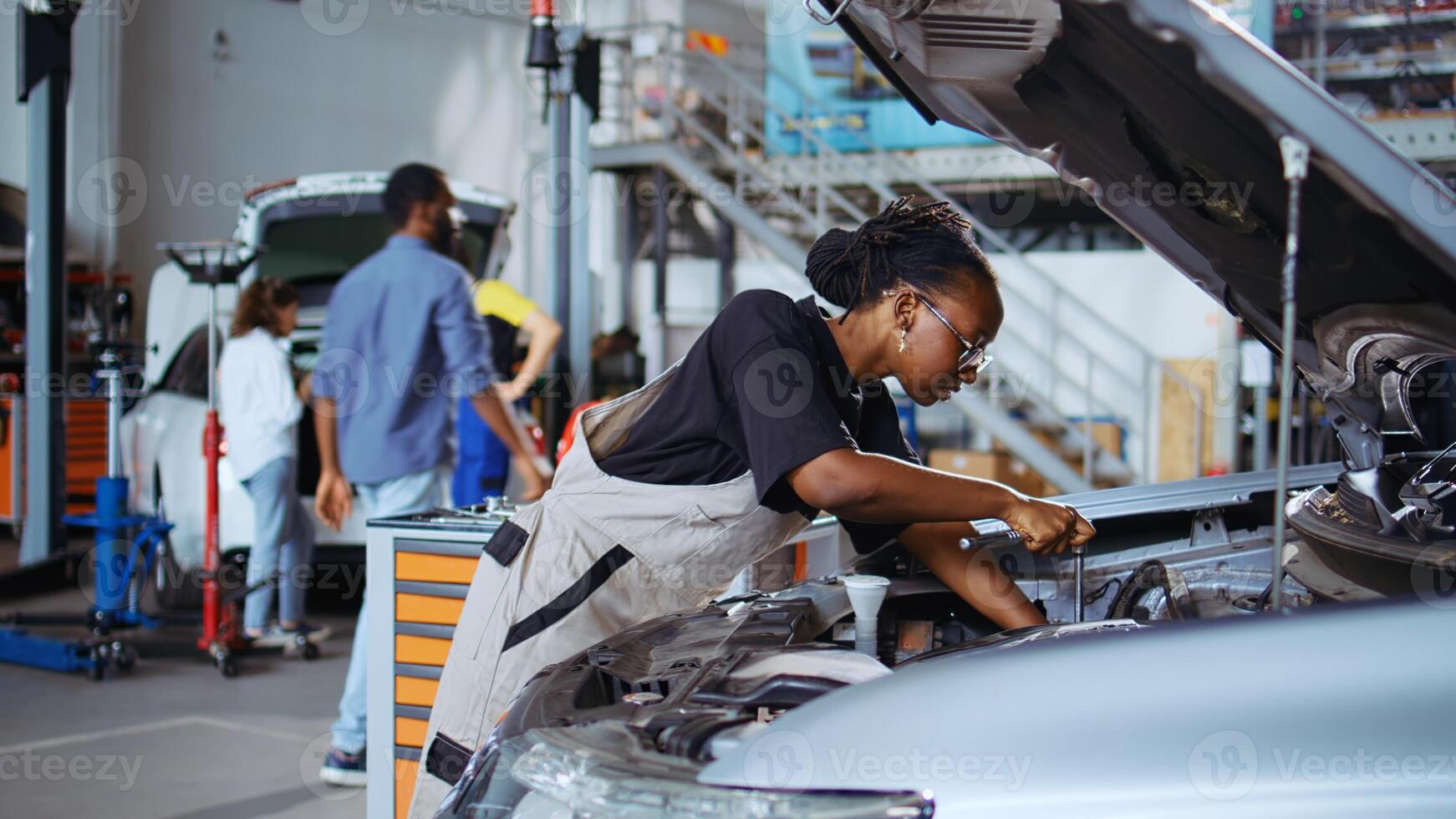 Repair shop workers using torque wrench and screwdriver to fix car in need of repairments. Colleagues servicing broken vehicle, checking for oil leakage using professional tools photo