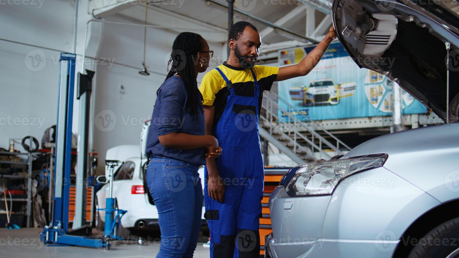 Certified serviceman listens to customer in repair shop, using tablet to write down car modifications needed. Specialist in garage workspace with client, listening to her requests for vehicle tuning photo