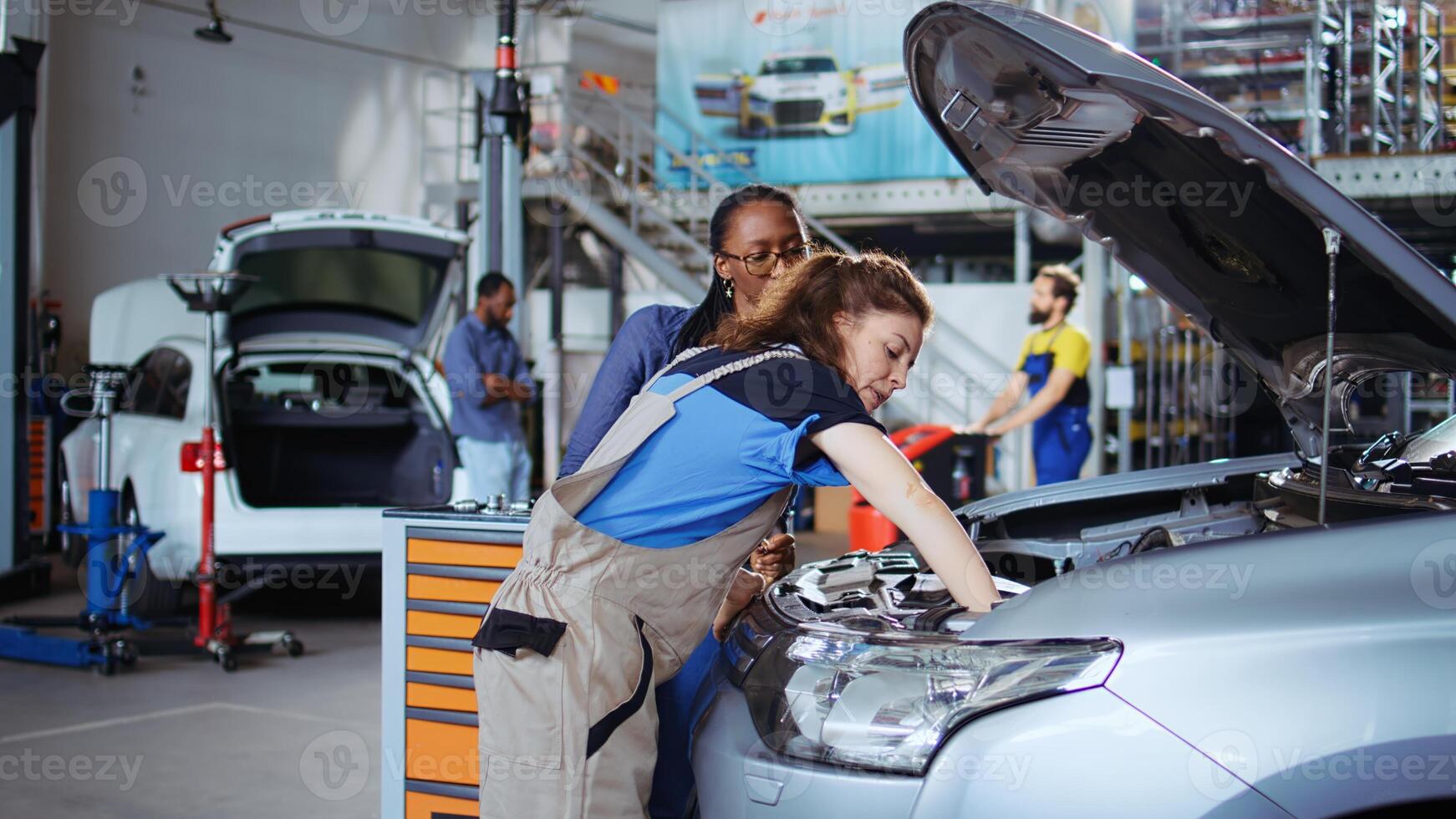 Licensed technician in garage finishing fixing car for customer, looking underneath vehicle hood to remove remaining oil leaks. Expert does annual parts cleaning on client automobile in repair shop photo