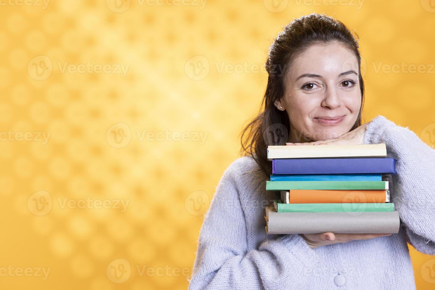 Portrait of happy woman holding pile of books, portraying reading blissfulness concept, studio background. Cheerful book lover hugging stack of novels, showing appreciation for literature photo
