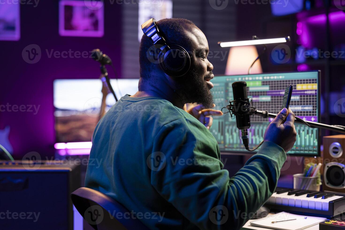 Skilled artist performing his new song for the acoustic version in home studio, recording his track on microphone and reading the lyrics on his smartphone. Songwriter producing cool music. photo