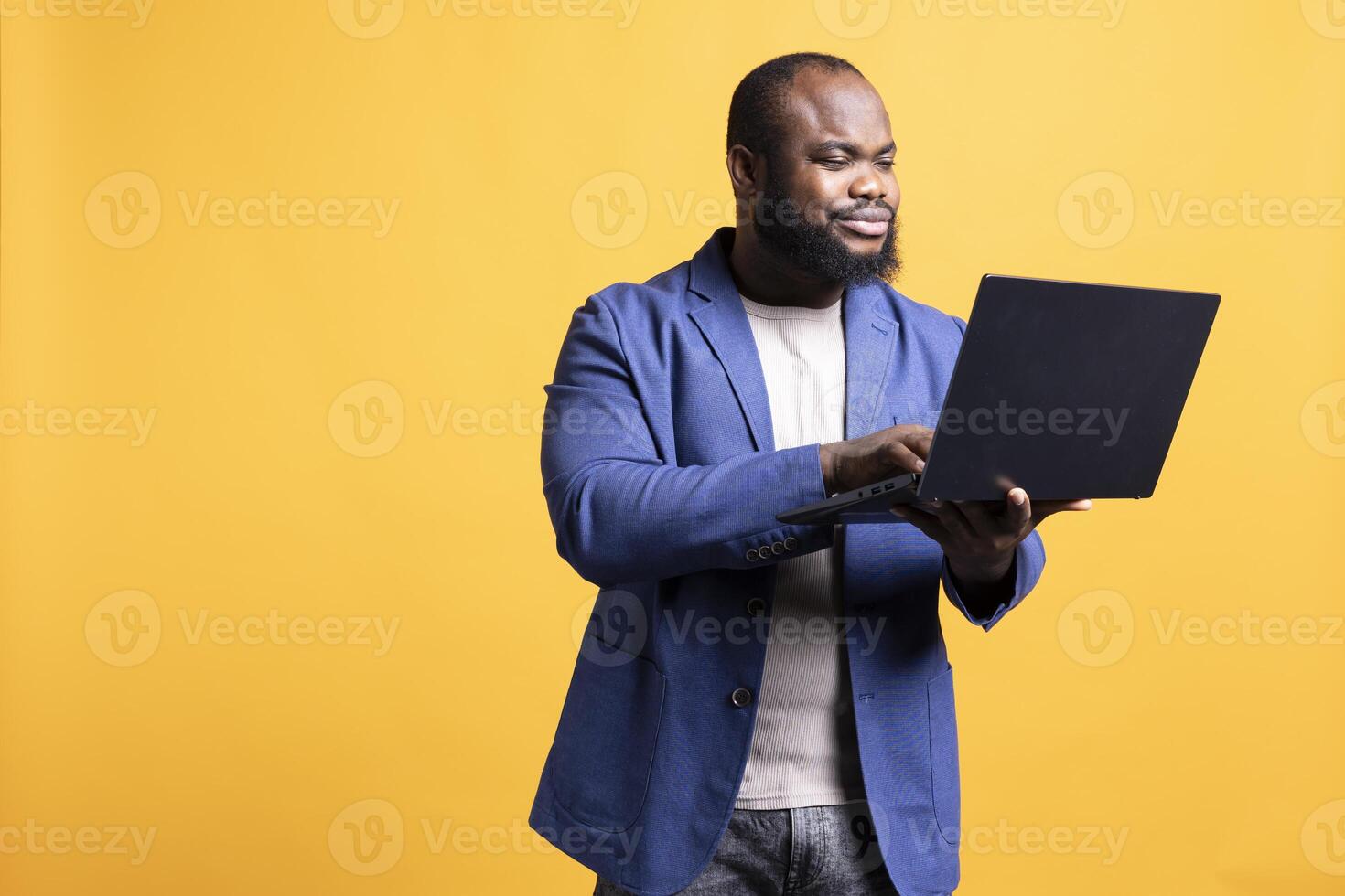 Smiling african american man looking at business diagram and figures on laptop, isolated over studio background. Upbeat worker checking company financial annual report charts on notebook photo