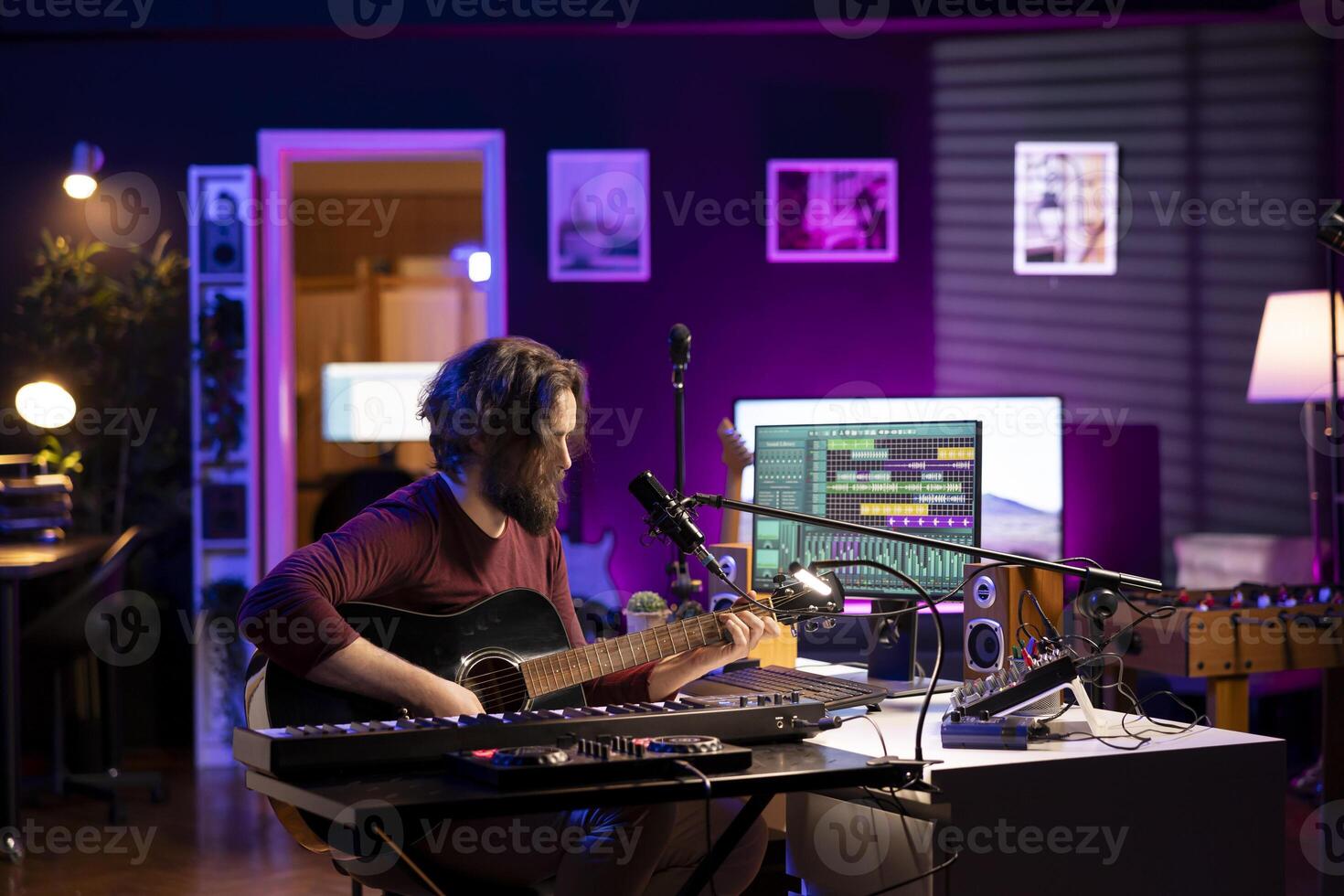 Songwriter artist producing sounds with acoustic guitar and equalizer in his home studio, using a microphone to sing the chords. Music producer composing new tunes with soundboard controls. photo