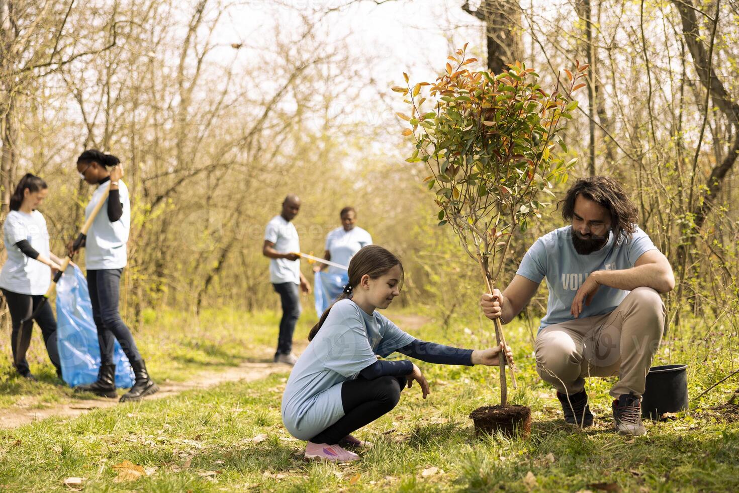 Man and young kid volunteering to fill a hole with a tree, working on reforestation mission together. Proud father and daughter planting greenery to increase forest vegetation. photo
