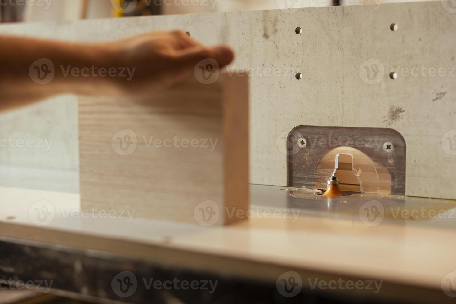 Man putting lumber block through spindle moulder, creating smooth and precise edges on wooden pieces. Joiner using heavy machinery to craft strong and seamless joints for furniture and structures photo