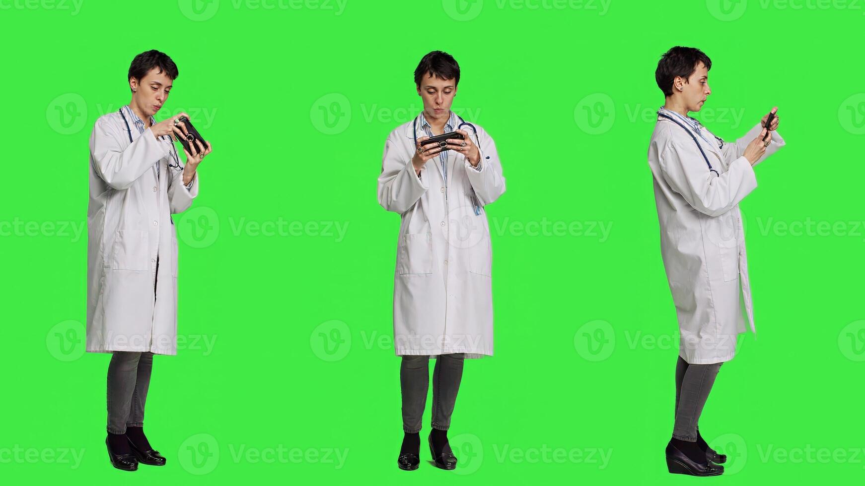 General practitioner playing games on mobile phone app, having fun with online gaming competition against greenscreen backdrop. Cheerful doctor relaxing with internet game. Camera A. photo