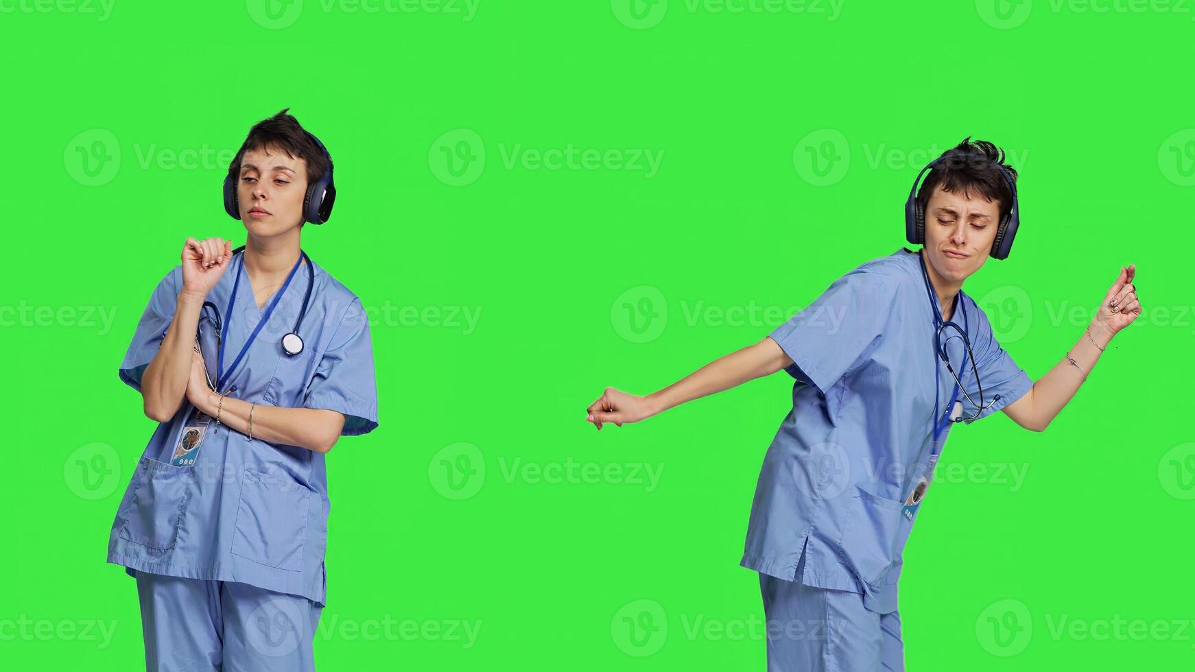 Cheerful health specialist listening to cool music on audio headset, dancing against greenscreen backdrop and having fun. Nurse enjoying songs an doing funny dance moves, leisure. Camera B. photo