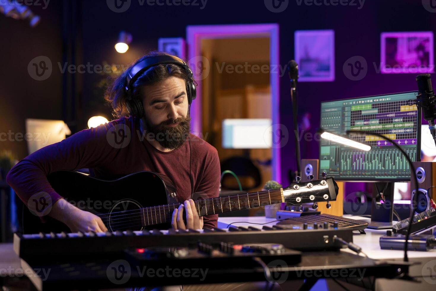 Producer composing music with his acoustic guitar in home studio, recording acoustical tunes on strings and singing melody. Audio engineer mixing and mastering his song with production gear. photo