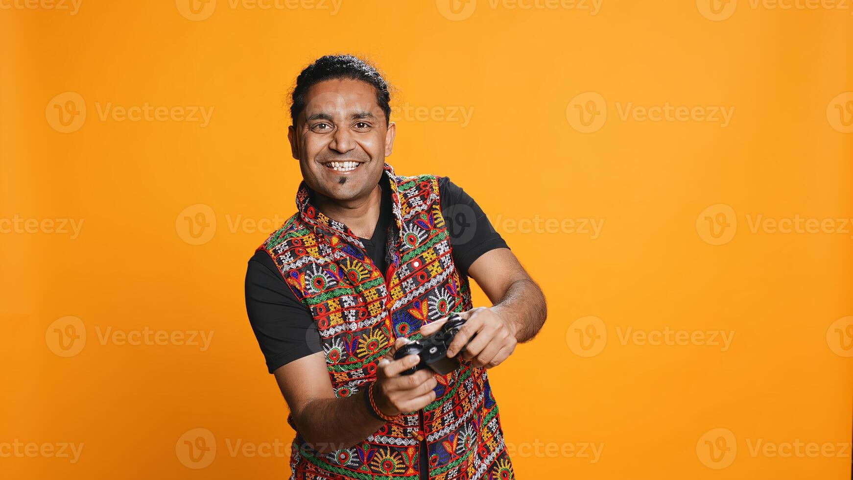 Happy gamer celebrating after winning game on gaming console, studio background. Delighted Indian man bragging after being victorious in videogame, defeating all enemies using gamepad, camera B photo