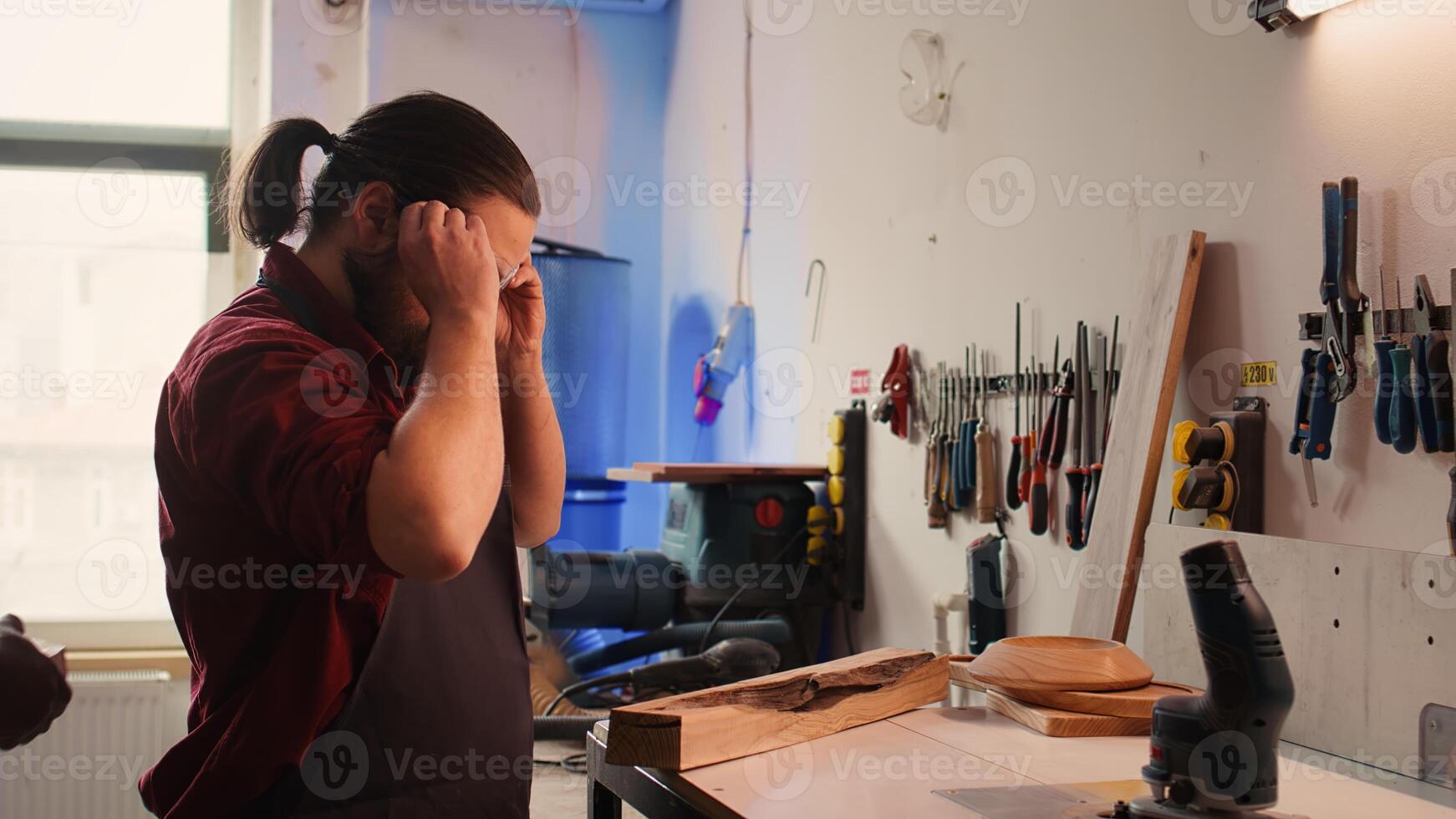 Manufacturer putting safety goggles on while selecting quality wood materials meeting client commission requirements. Woodworking expert doing quality assurance on timber block, camera B photo