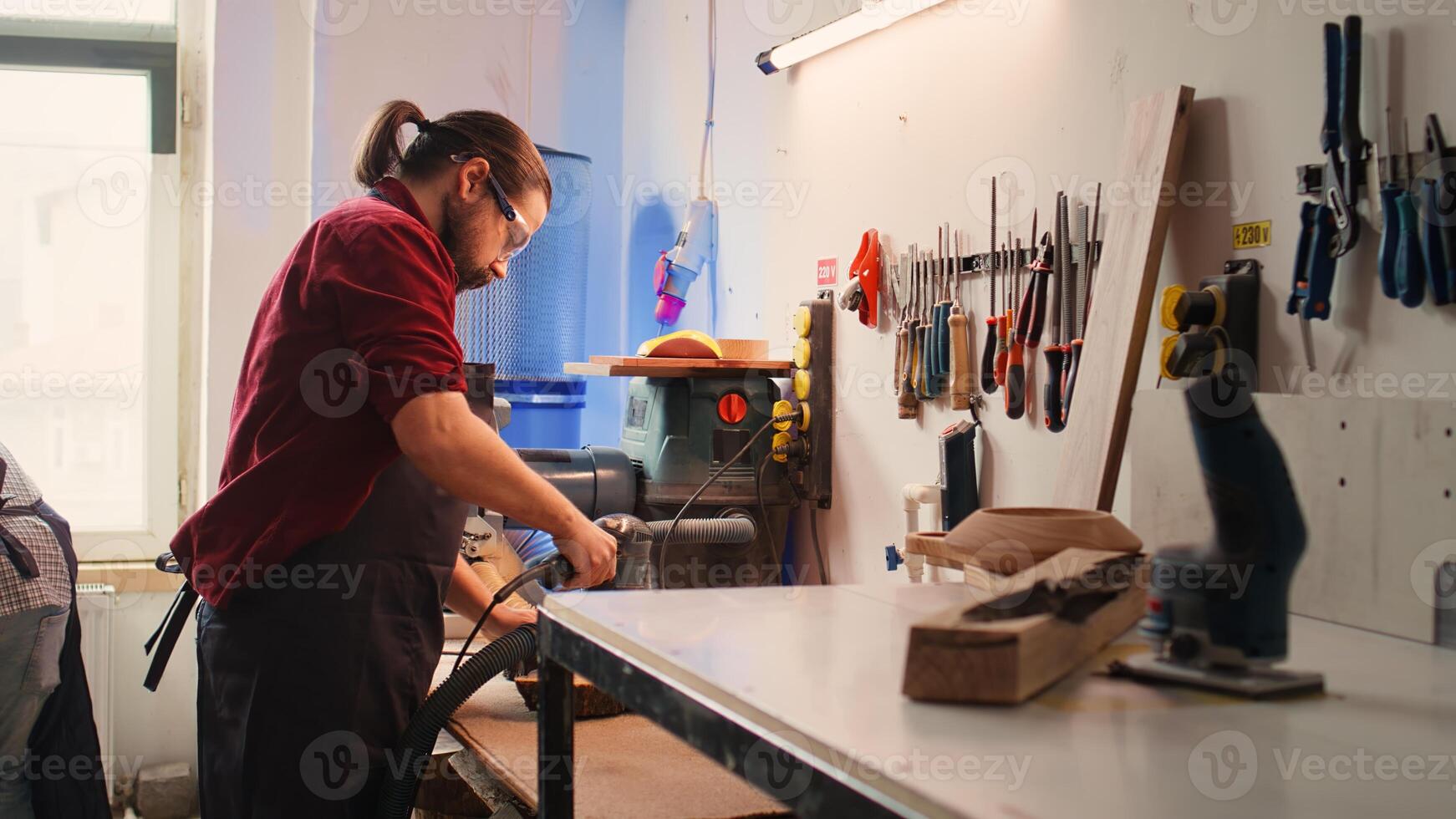 Carpenter collaborating with apprentice, using orbital sander with fine sandpaper to achieve refined finish. Manufacturer and BIPOC colleague using angle grinder on wood block, camera B photo