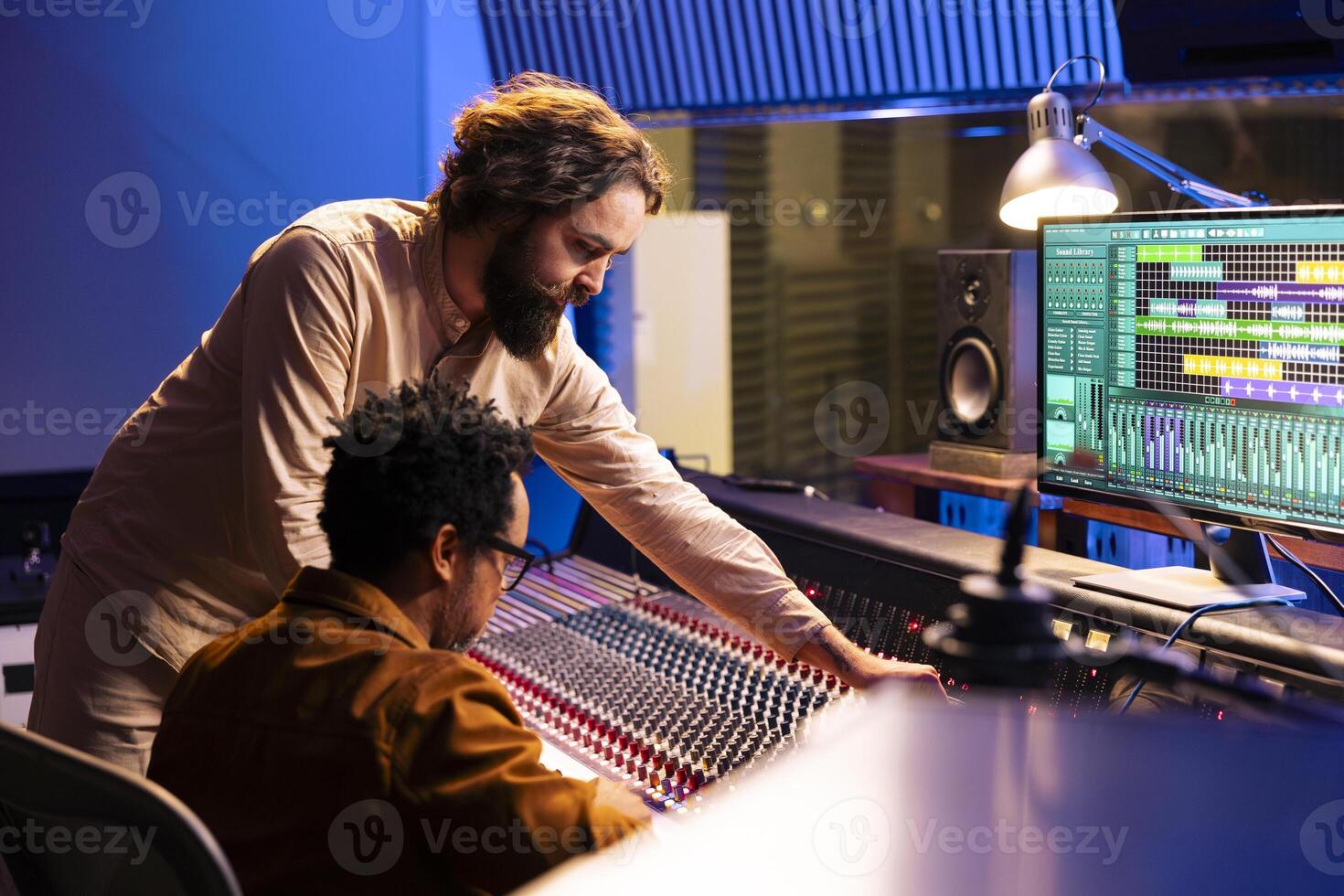 Diverse team of artist and audio engineer composing a hit song, working in professional music studio with technical gear. Musician with expert editing and recording music on mixing console board. photo