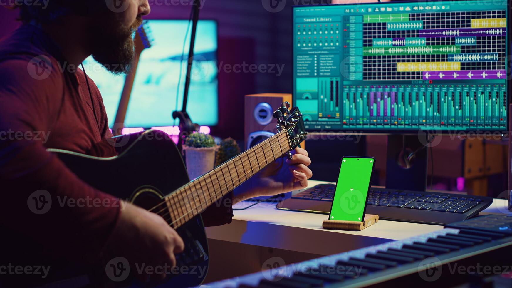 Young musician watching tutorial lesson to tune his guitar strings, looks at greenscreen layout on phone. Artist learning to play acoustic instrument, practicing on online musical class. Camera A. photo