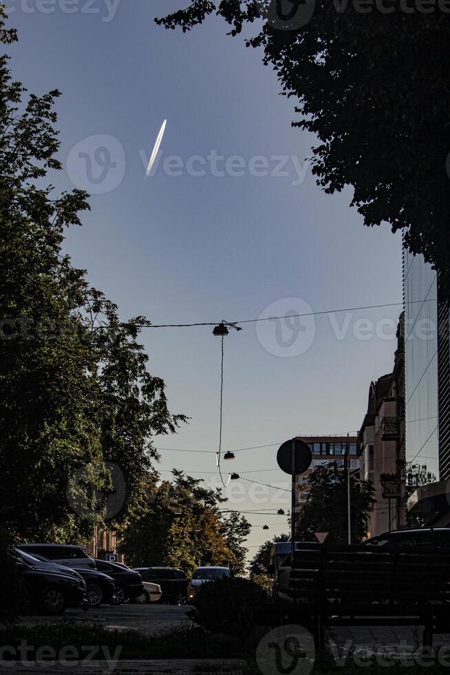Plain trail looking like meteor or shooting star going up on blue evening sky over city street in shadow photo