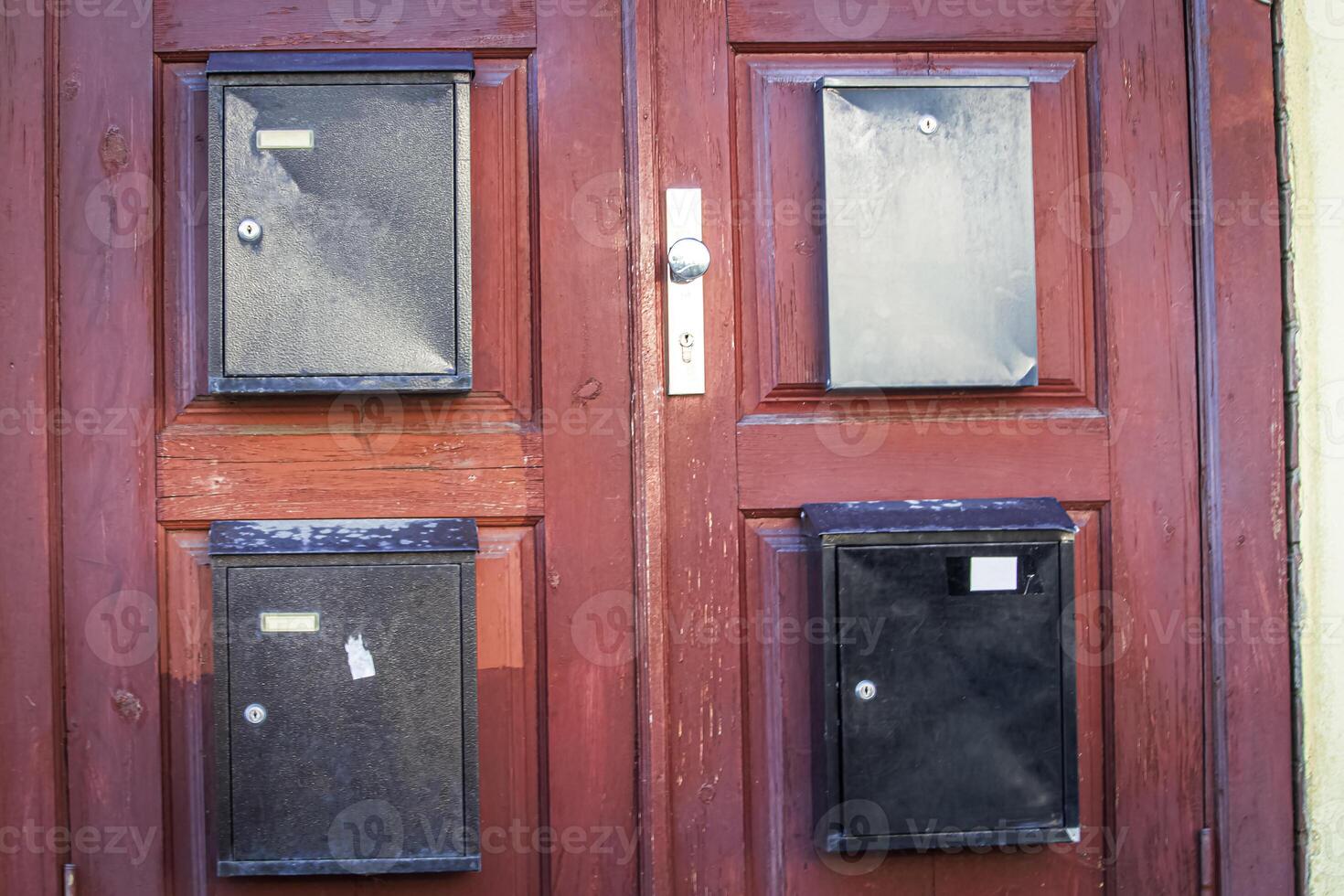 An exterior red wooden door of a residential building with multiple small square glass panes and four old mail boxes photo