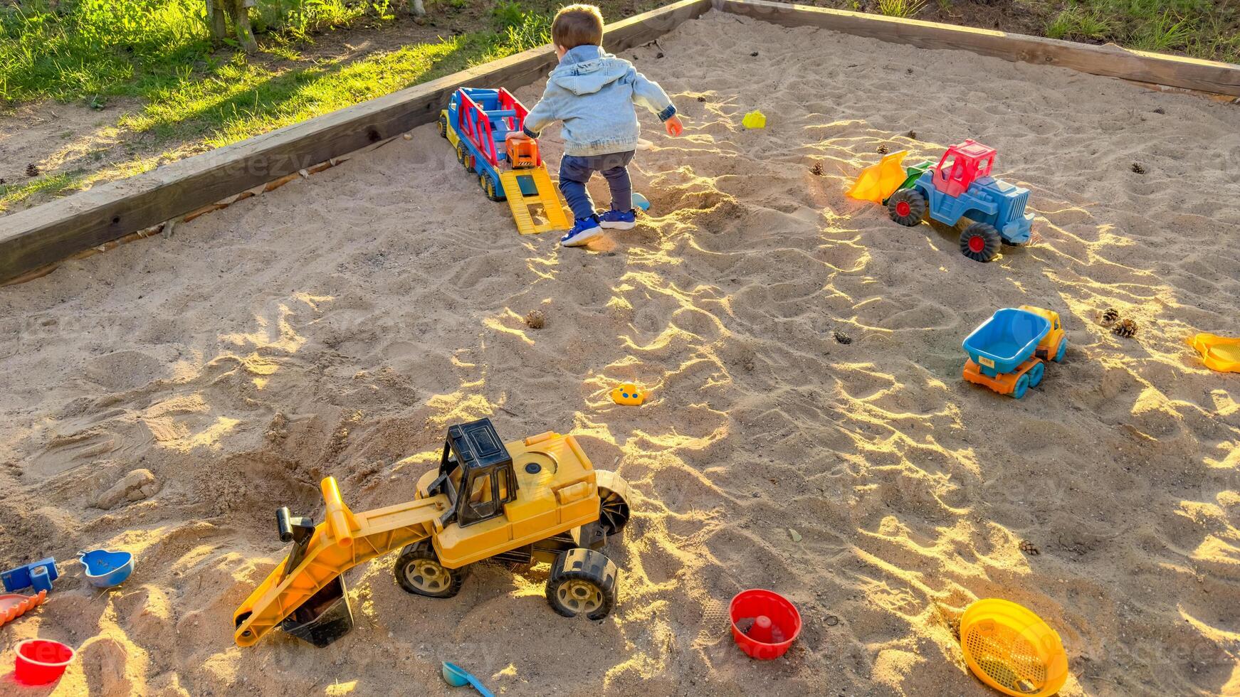 Child playing with toys in sandbox. Boy having fun on playground in sandpit photo