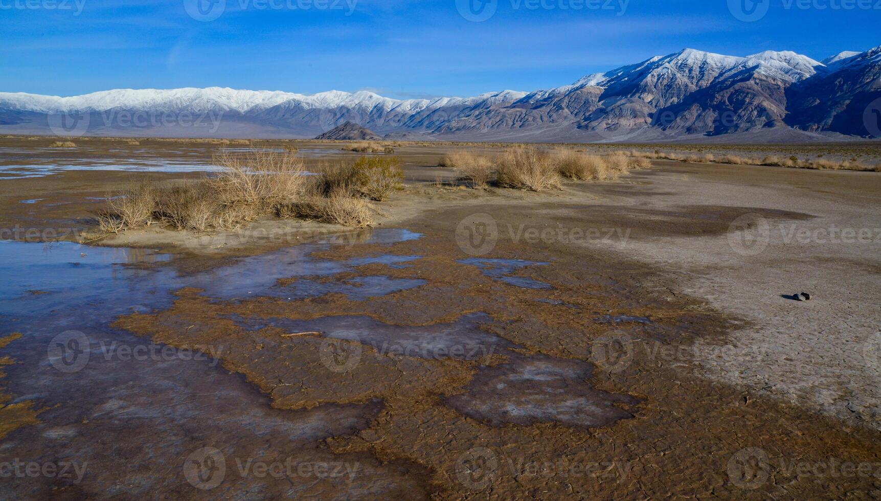 Landscape of wet clay desert in winter against the backdrop of snow-capped mountains in the Death Valley area photo