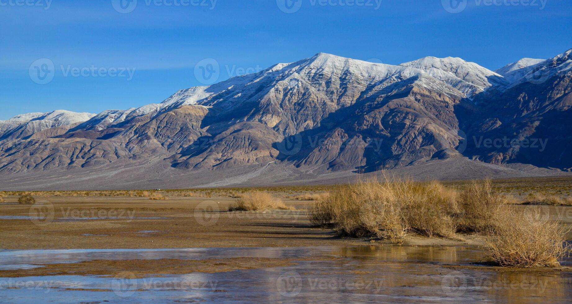Landscape of wet clay desert in winter against the backdrop of snow-capped mountains in the Death Valley area photo