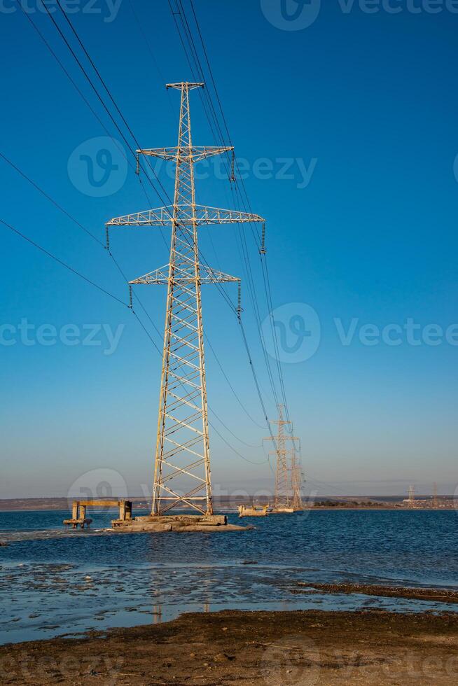 High-voltage power line against the background of the blue sky above the water of the lake photo