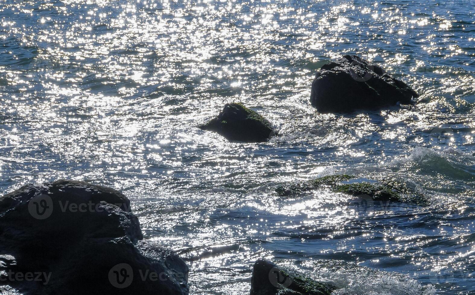 Bright reflections on the water on a sunny day among the coastal rocks near the Black Sea coast photo