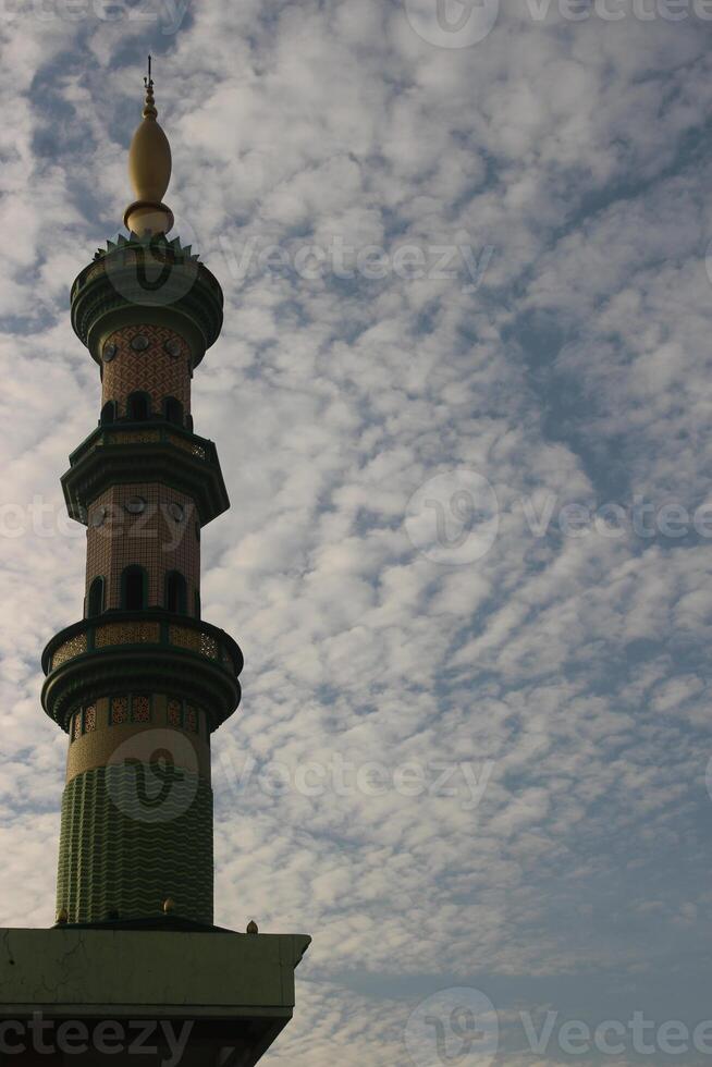 White and green mosque tower. Mosque tower with clouds in Indonesia background. photo