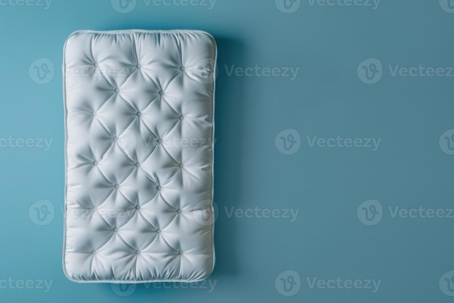 A cozy, tufted mattress resting against a serene blue wall in a minimalist bedroom setting photo