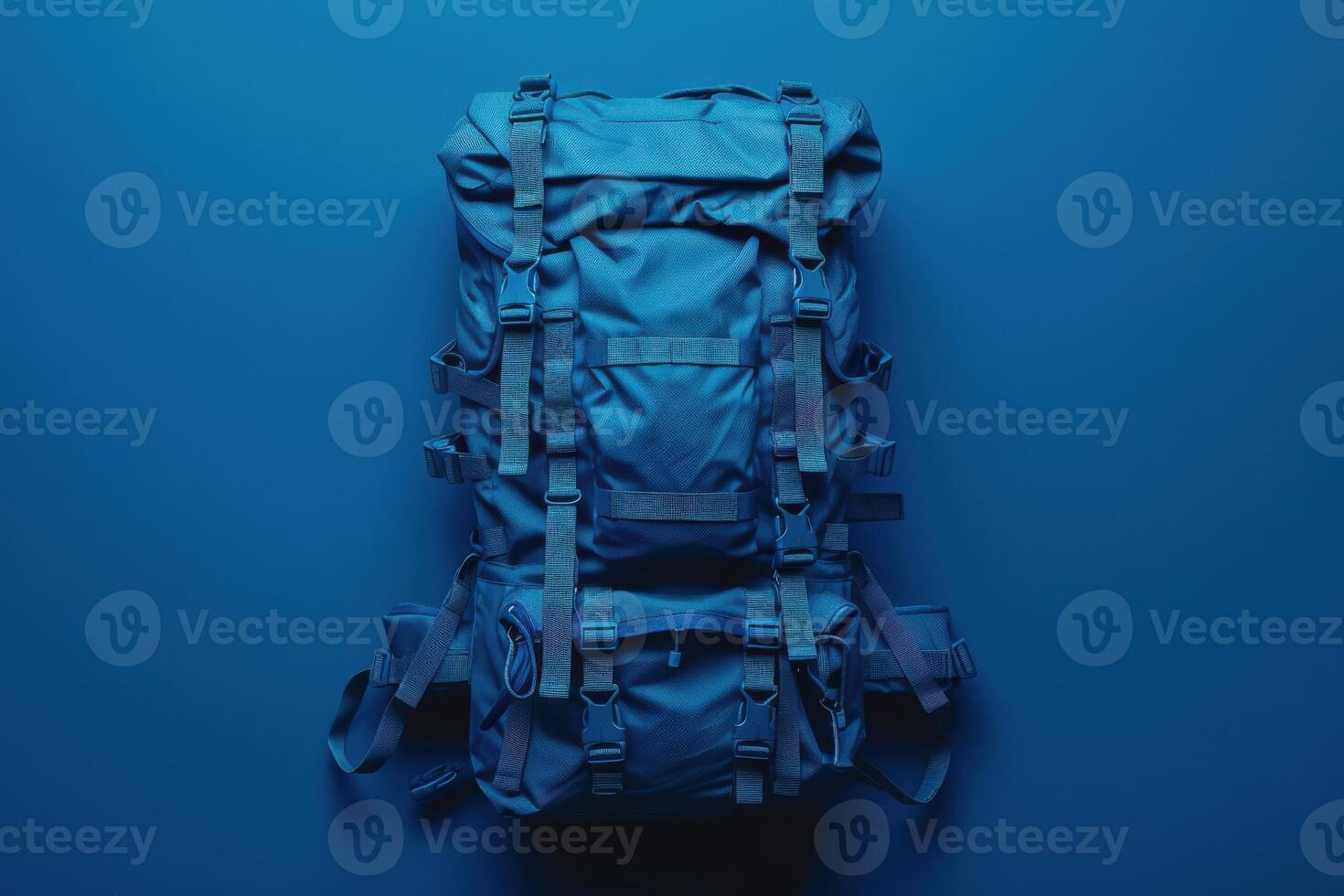 A vibrant blue backpack rests on a deep blue background, showcasing rugged straps and compartments, perfect for adventure or travel preparation photo