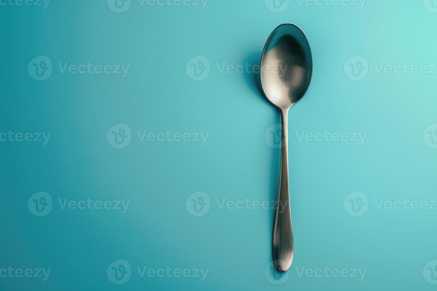 A sleek silver spoon resting against a vibrant turquoise backdrop, highlighting simplicity and elegance in everyday objects photo