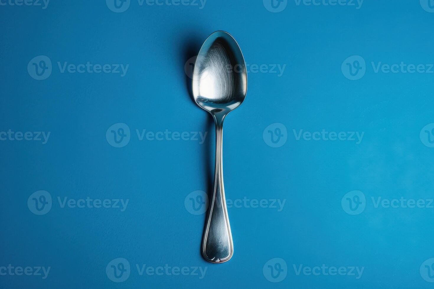 A shiny silver spoon rests gracefully on a vibrant blue background, glimmering in soft light, inviting thoughts of culinary delights and shared meals photo