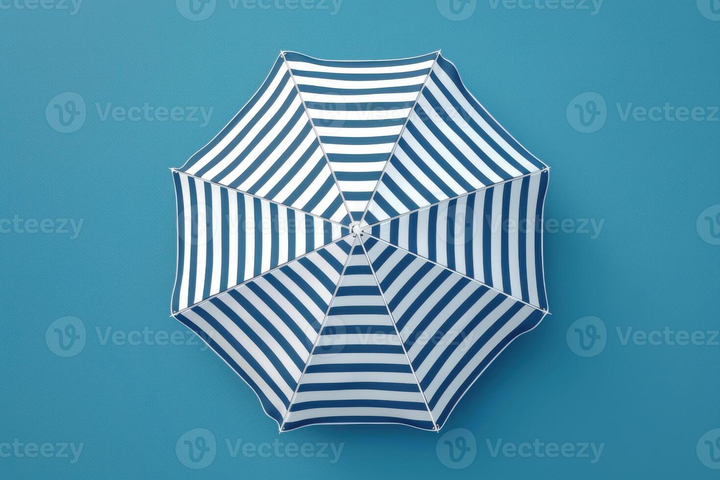 A vibrant blue and white striped umbrella rests against a solid blue background, evoking summertime relaxation and beach days photo