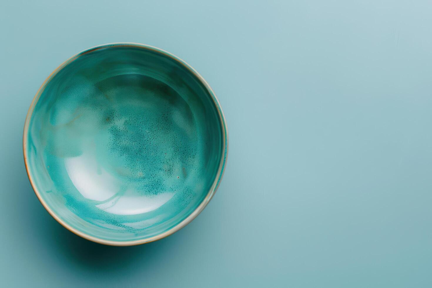 A serene teal bowl resting on a smooth aqua surface, showcasing intricate watercolor patterns photo