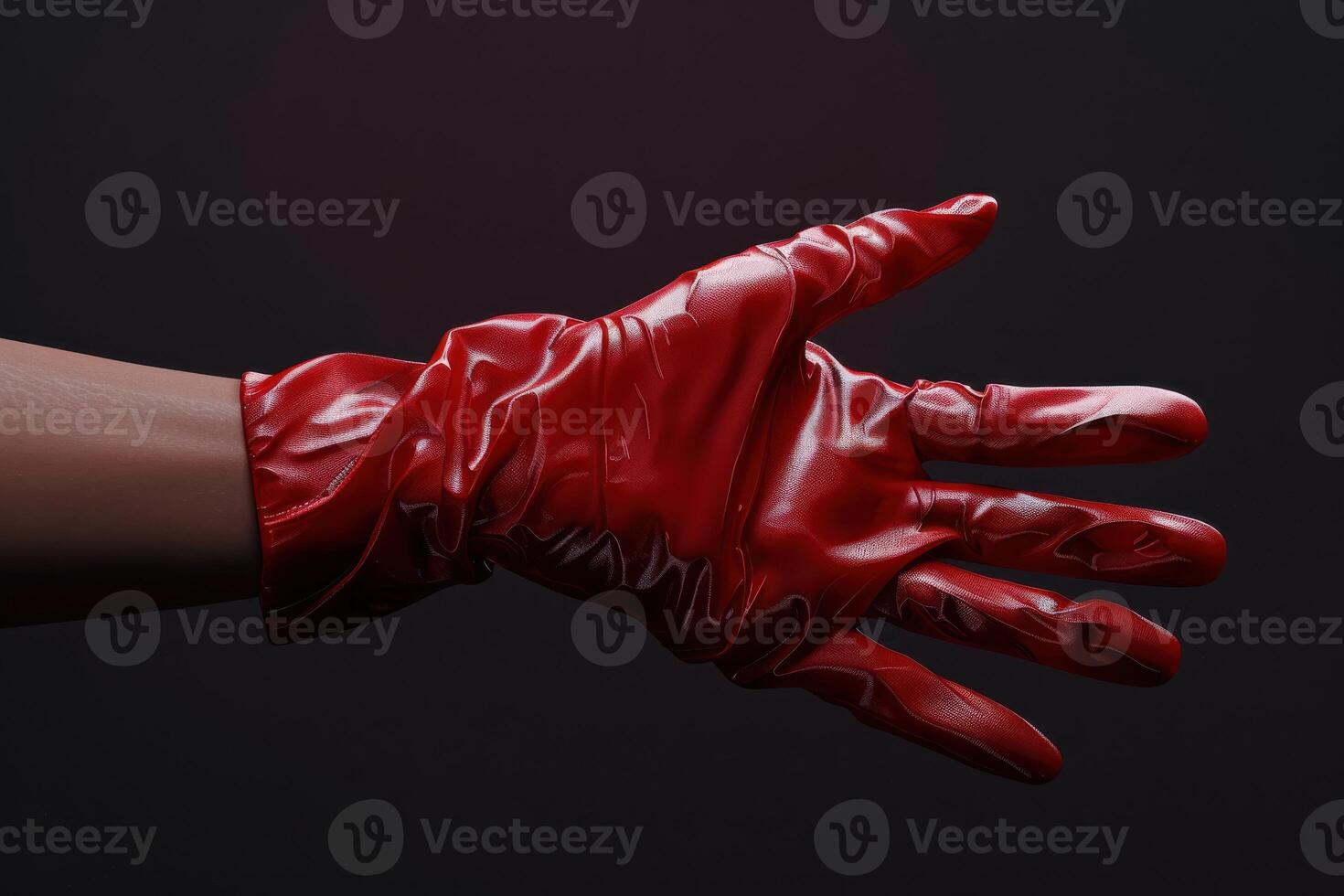 A close-up of a gloved hand wearing a shiny red latex glove against a dark background photo