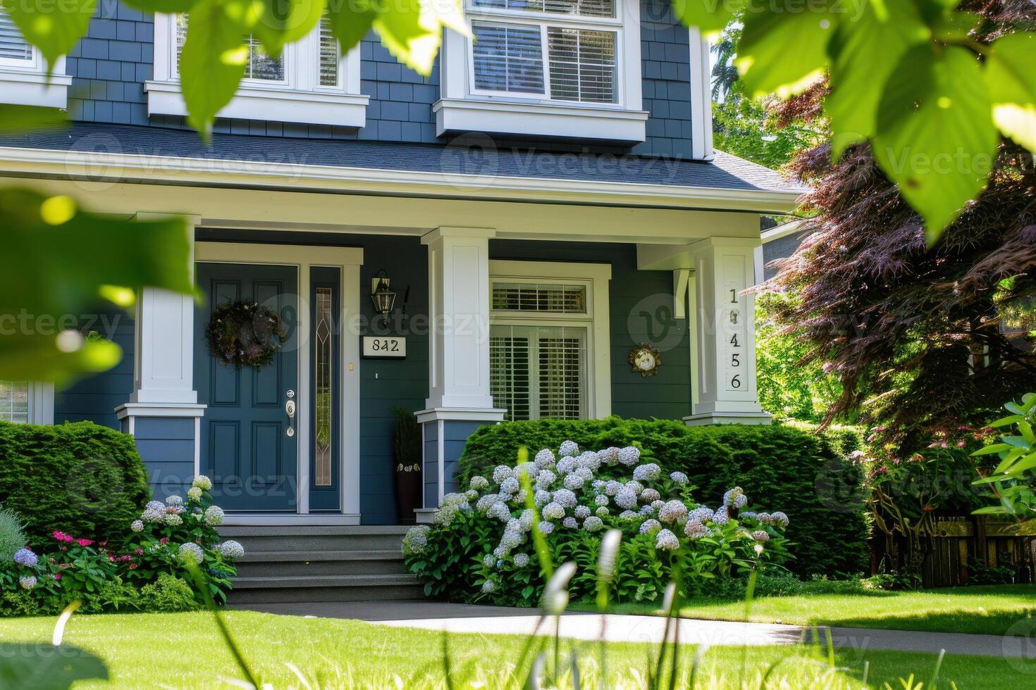 A charming blue house with white trim and a welcoming front porch surrounded by lush greenery in the suburbs on a sunny day photo