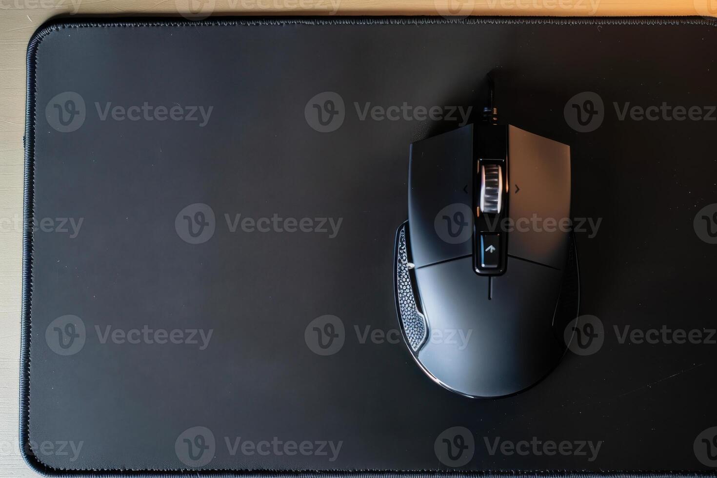 A wireless gaming mouse positioned on a black mouse pad in a well-lit workspace during the afternoon photo