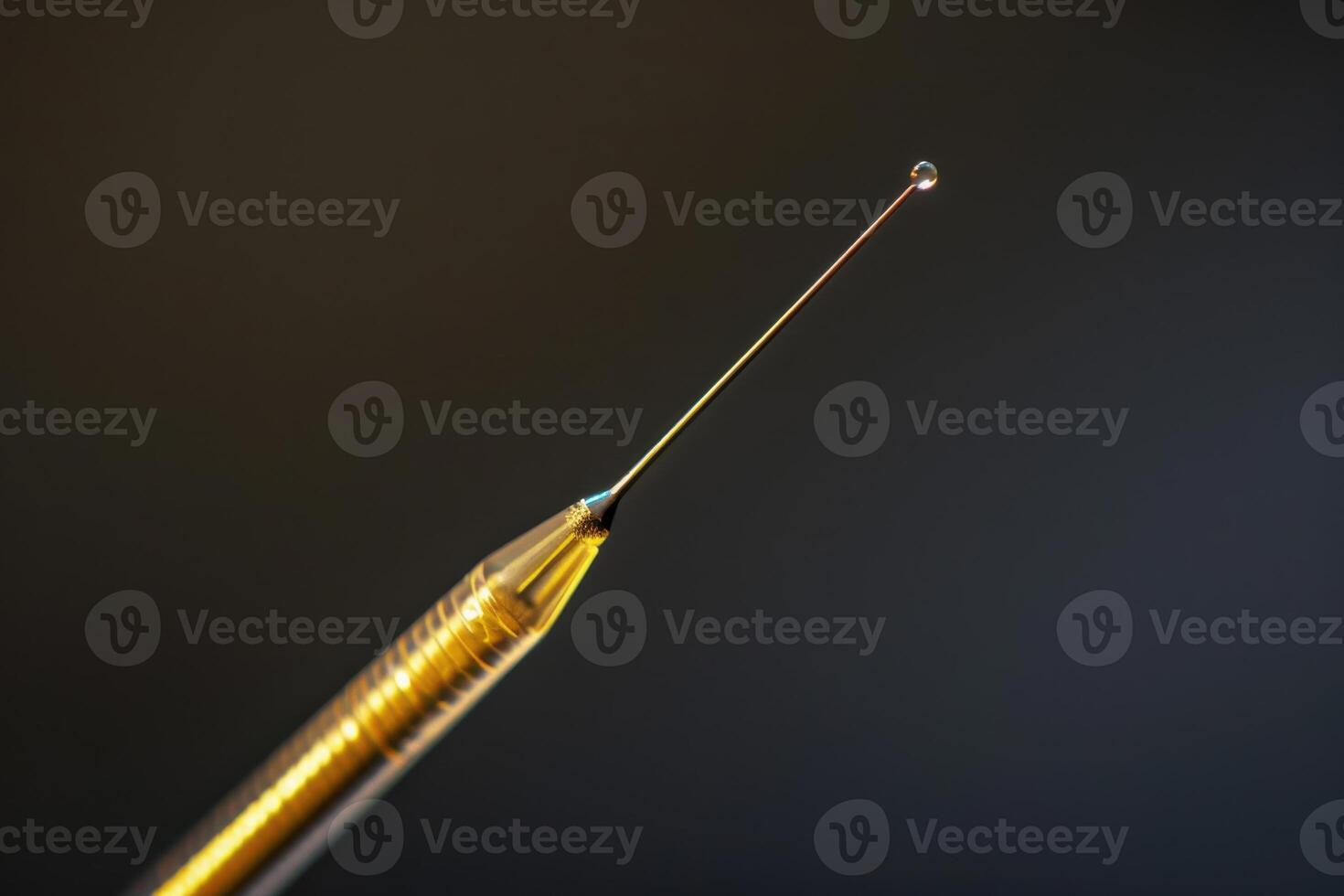 A close-up of a needle tip with a droplet of liquid poised at the end, illuminated against a dark background photo
