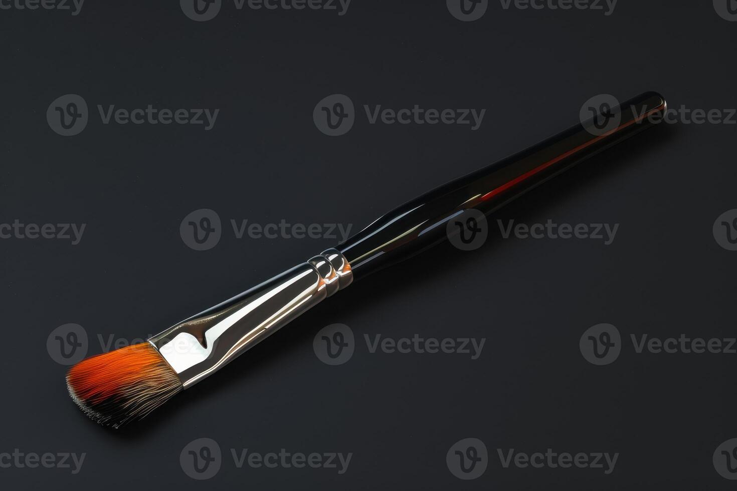 A professional makeup brush with a vibrant orange tip on a dark background photo