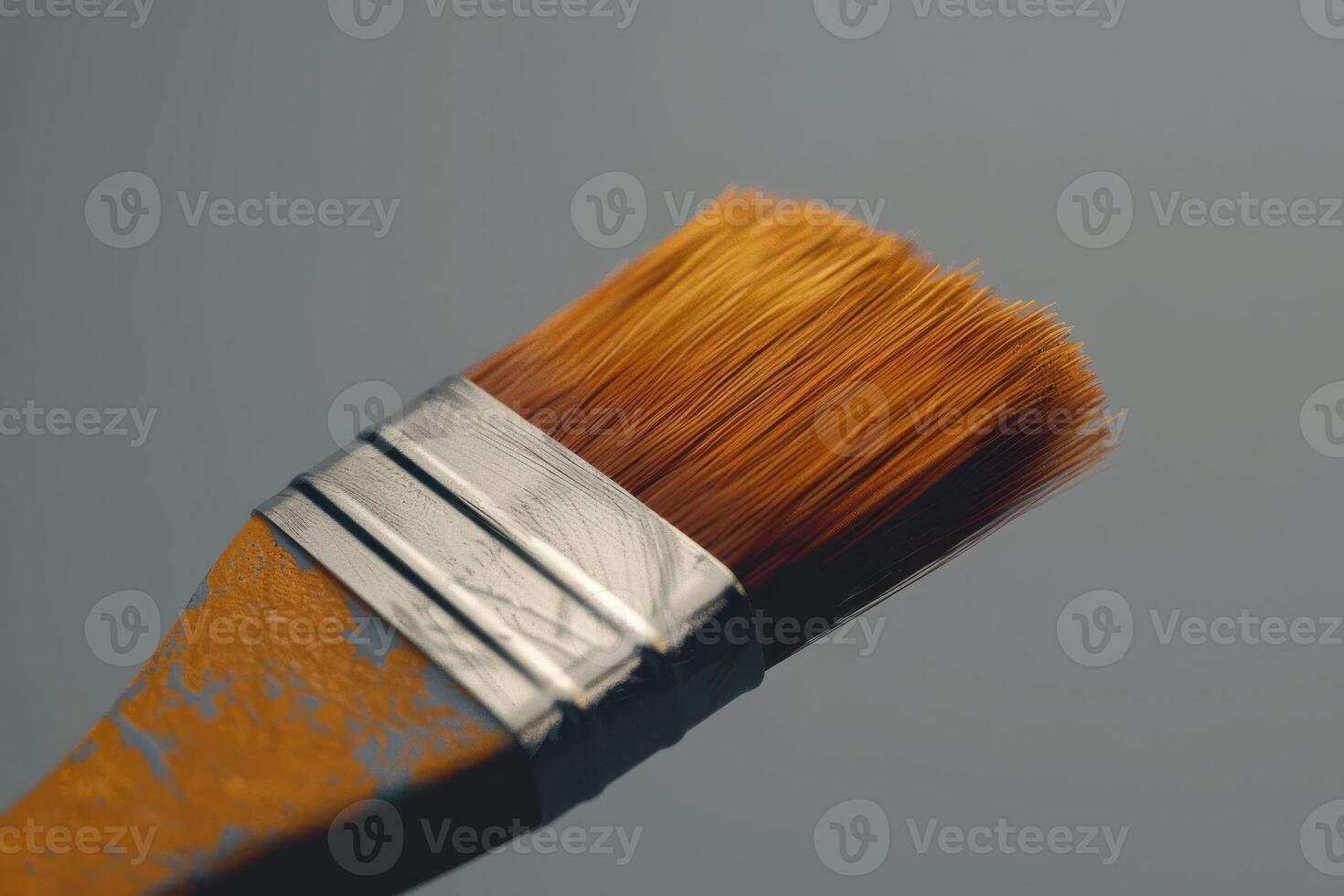 Close-up of a paintbrush with orange bristles resting against a gray background after a painting session photo
