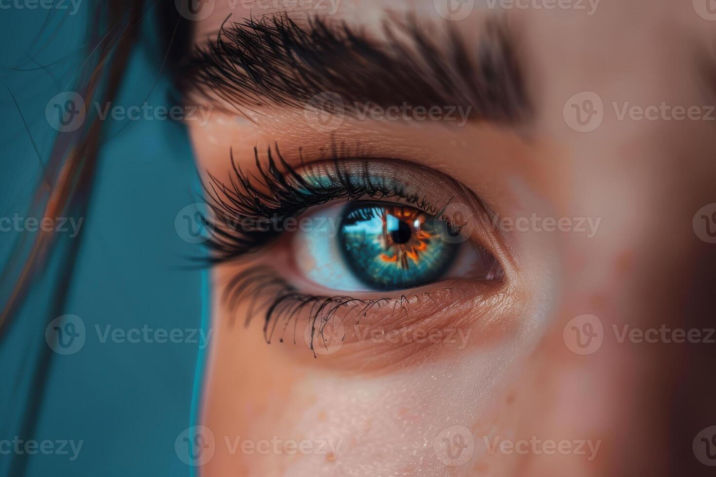 Close-up of a person's blue eye with reflections and defined eyelashes against a blue background photo