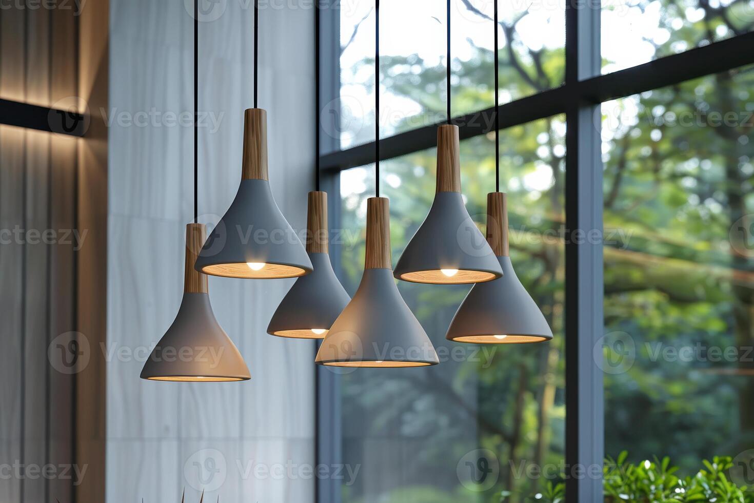 Elegant modern pendant lights hanging in a cozy interior space surrounded by large windows with greenery outside photo