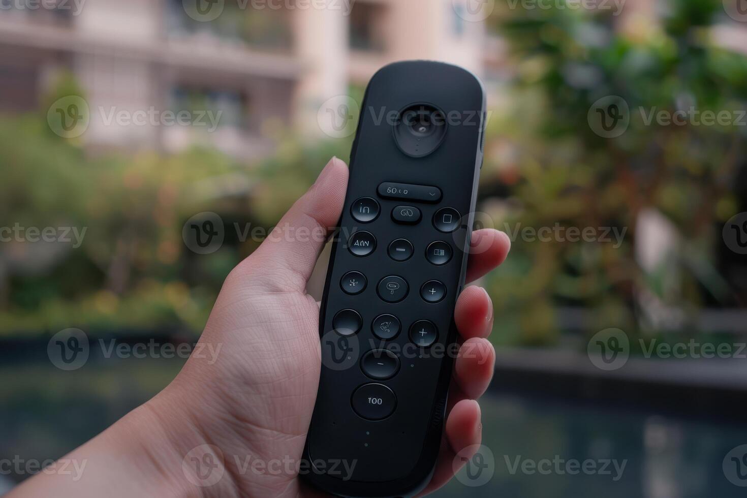 Person holding a black remote control near a pool in a lush garden during daylight photo