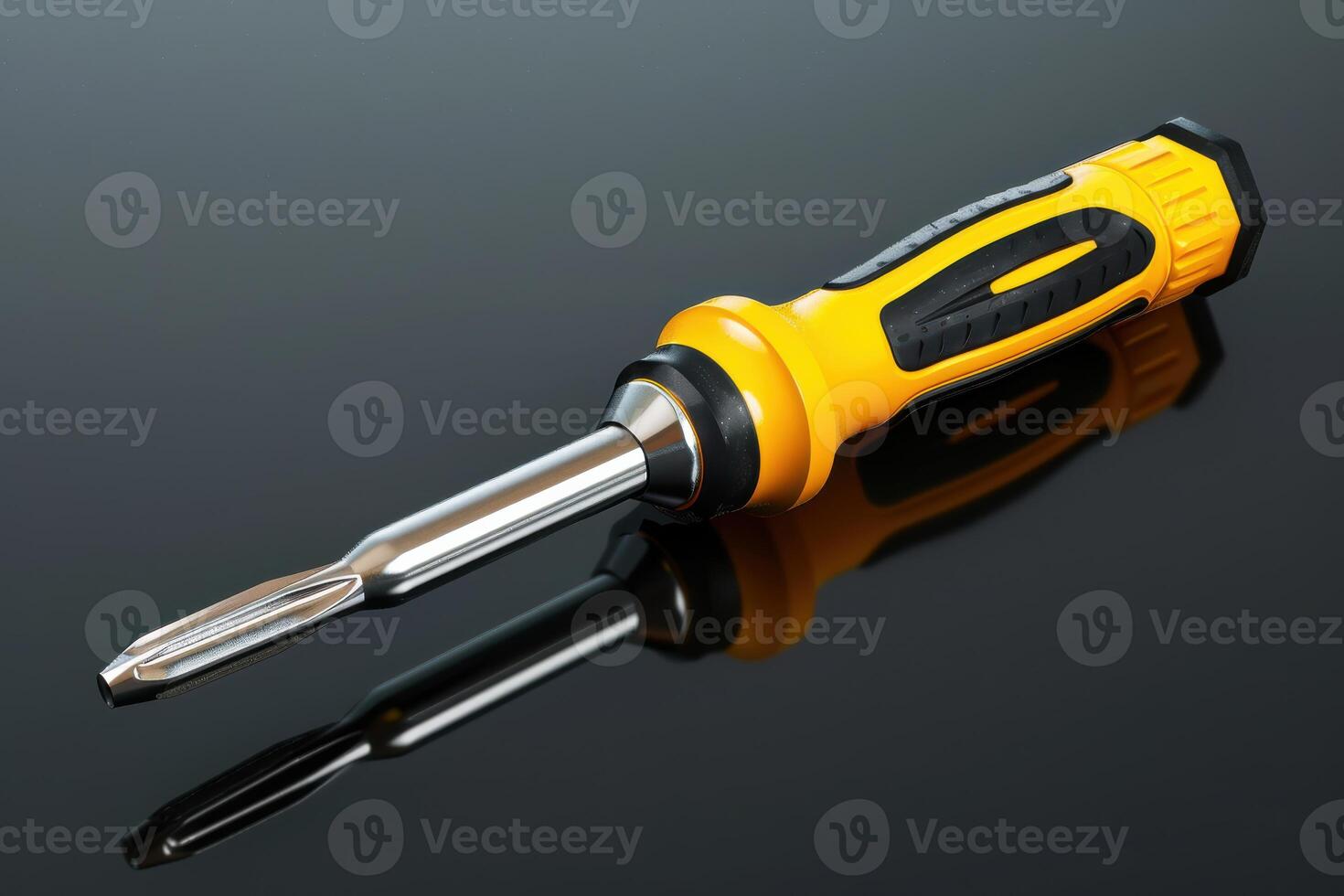 Close-up of a yellow and black screwdriver with a shiny metal tip resting on a reflective surface photo