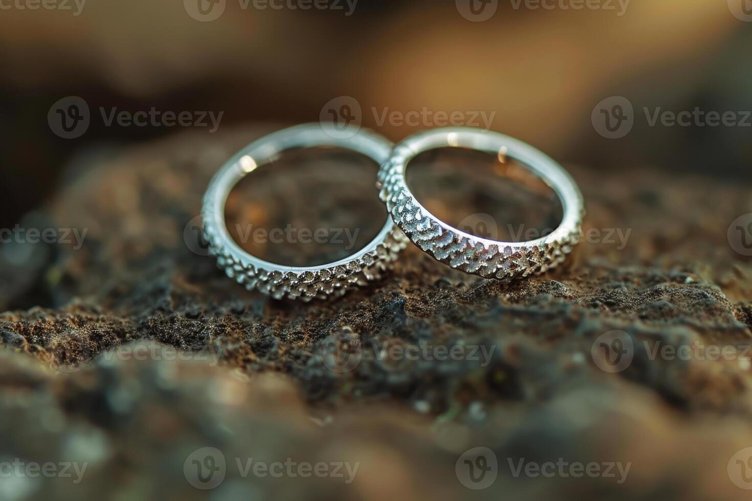 Close-up of two textured silver wedding rings resting on a rustic rock surface during sunset photo