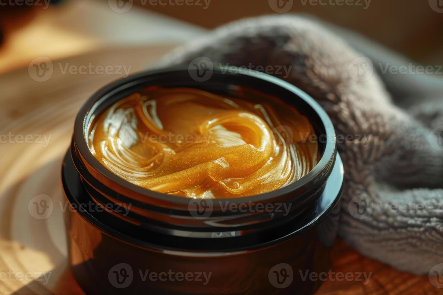 Golden cosmetic cream in a black jar with a soft towel in a warm setting photo