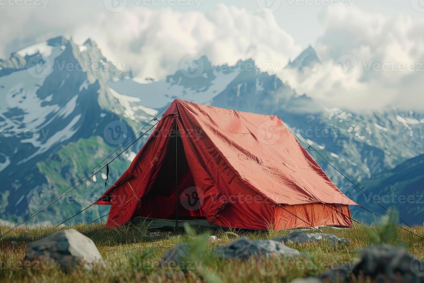 Bright red tent pitched in grassy field with mountains and clouds in the background during daylight photo