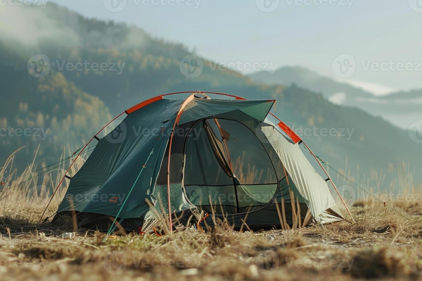 A camping tent set up in a grassy field against a backdrop of mountains during early morning light photo