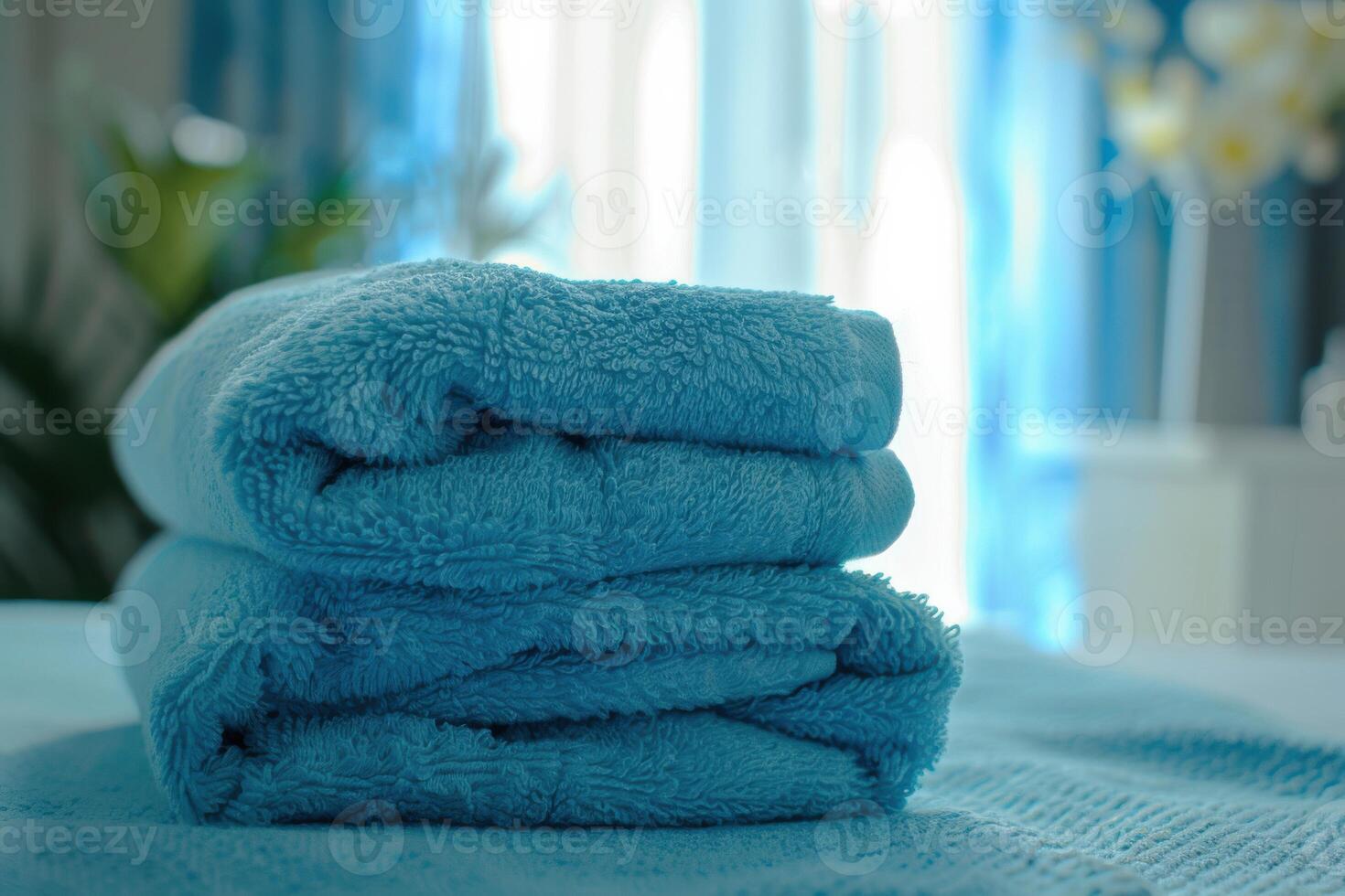 Soft blue towels neatly stacked on a bed in a bright, well-lit room during the afternoon photo