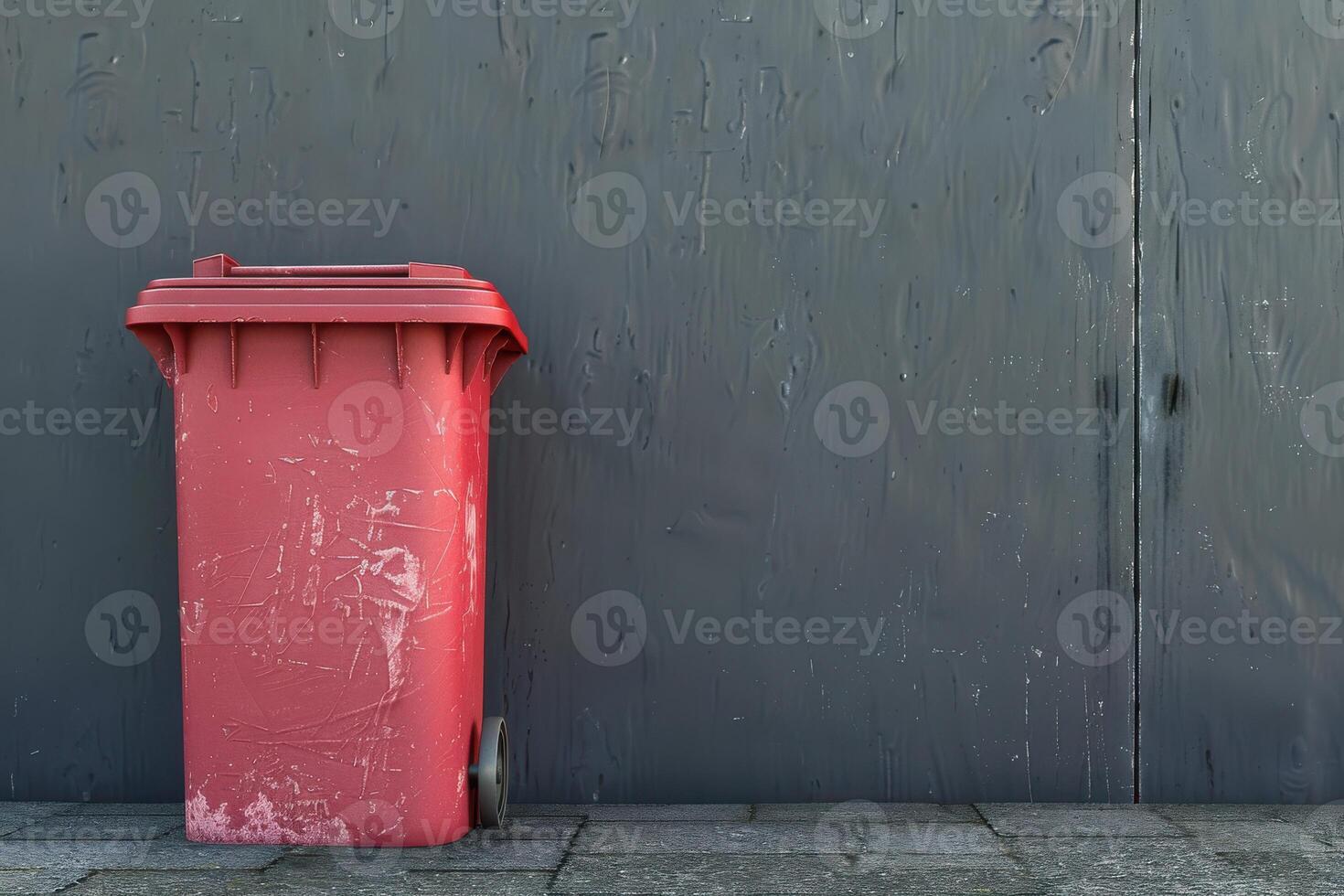 Red garbage bin against a gray wall in an urban alley during daylight photo