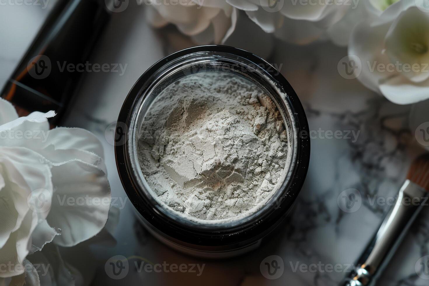 Powder in a jar surrounded by flowers and cosmetic tools on a marble surface photo