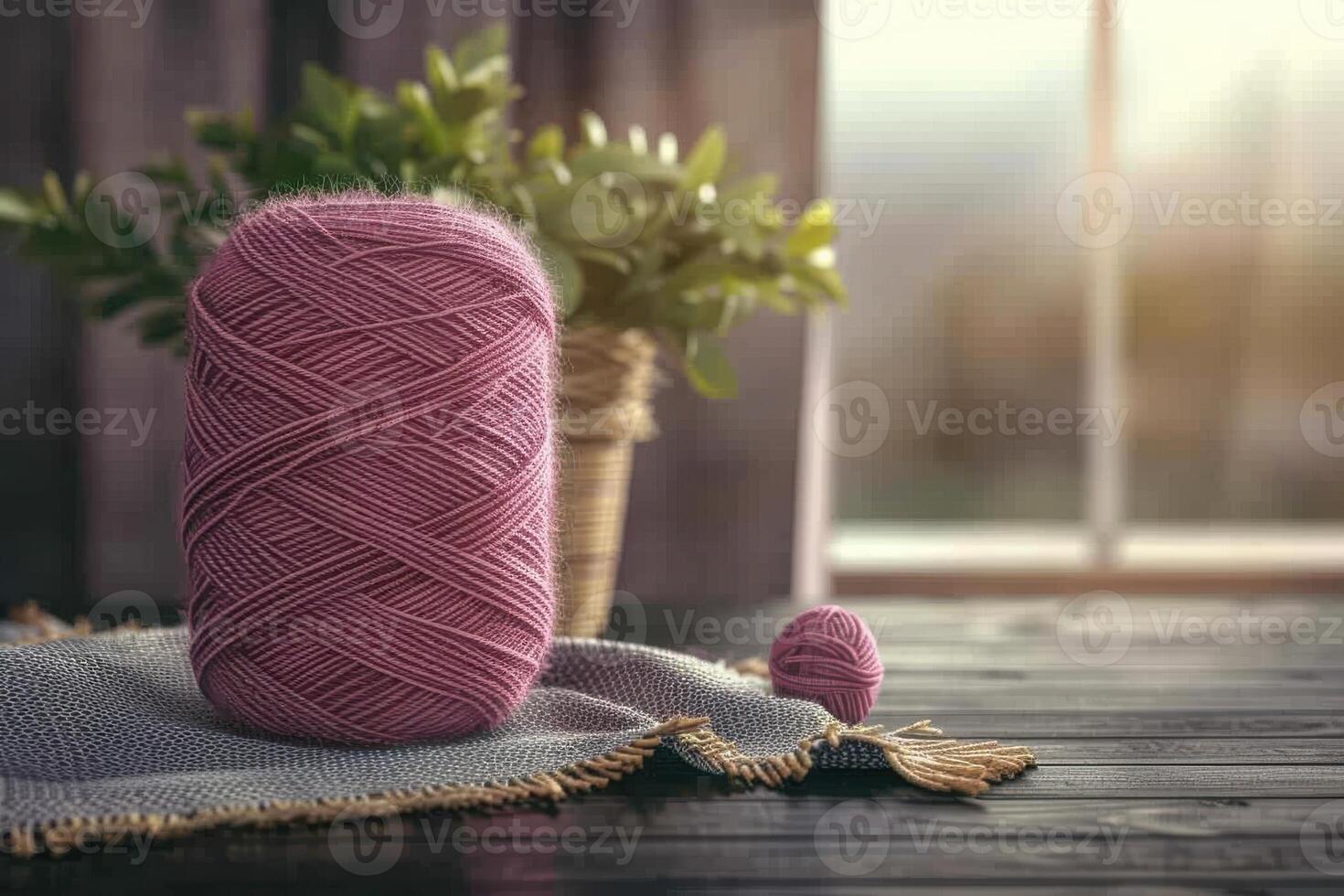 Soft pink yarn ball resting on a cozy knitted fabric near a sunny window with greenery in the background photo